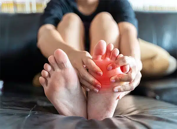 Close-up of a person sitting and holding their foot with a red glow indicating intense pain in the ball of the foot, showcasing symptoms of metatarsalgia or inflammation.