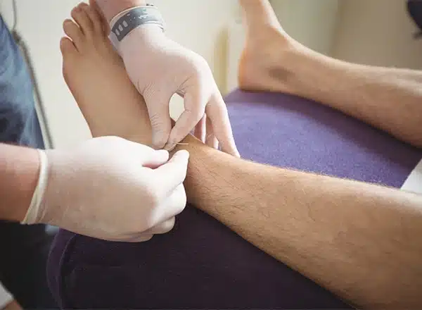A high-angle view of a caregiver's hands playfully holding a child's bare feet while they sit on a wooden window ledge.