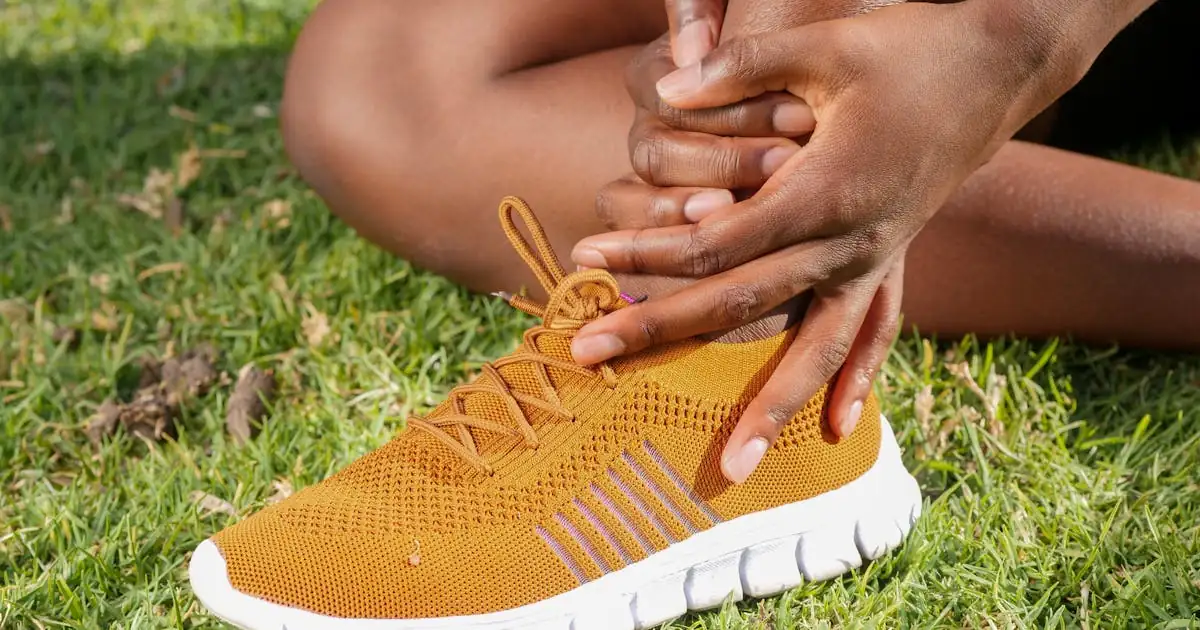 Athlete holding injured ankle on grass - ankle sprain rehab exercises, Balance Foot & Ankle Howell MI